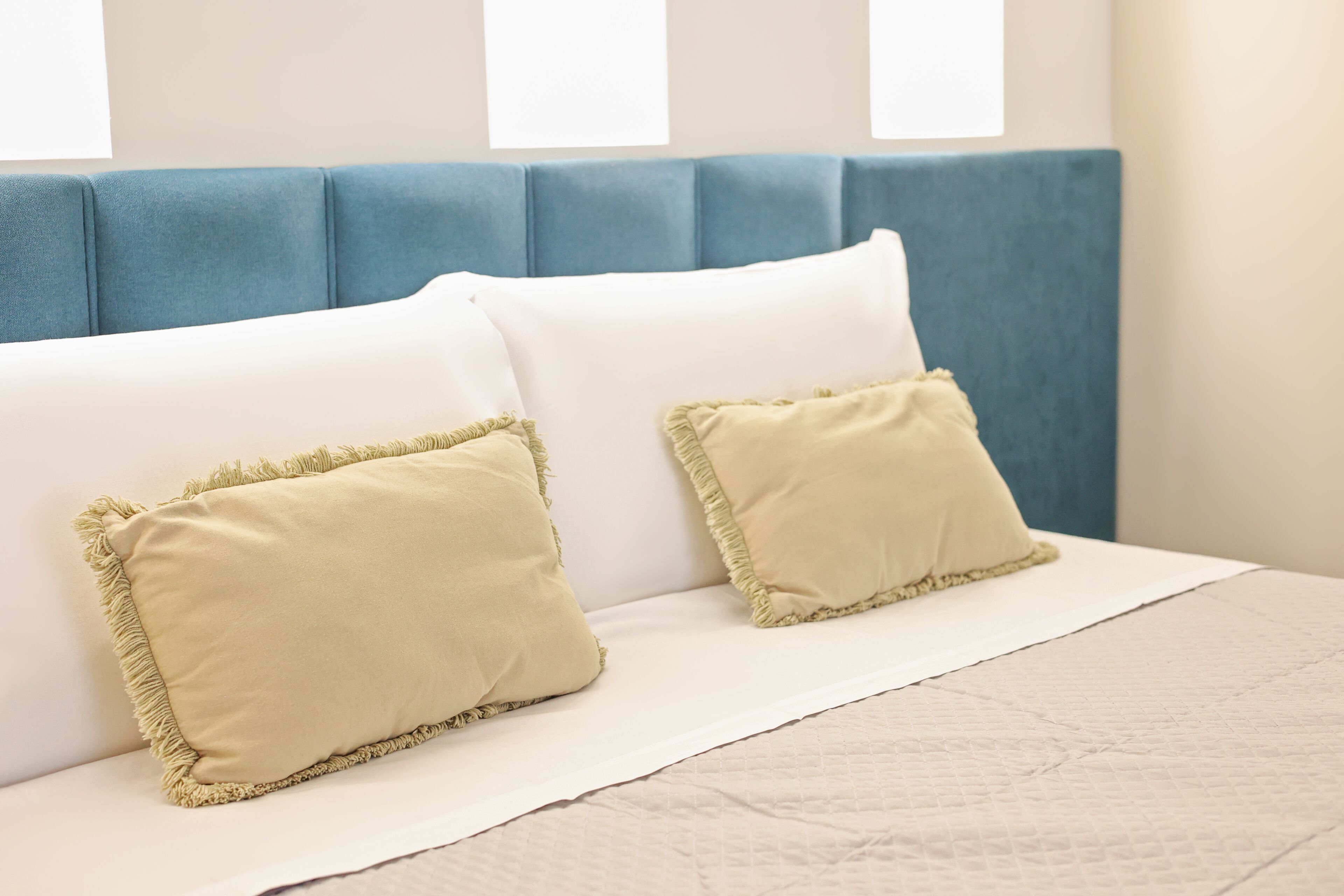Un letto con una testiera blu, due cuscini color beige e una coperta bianca.