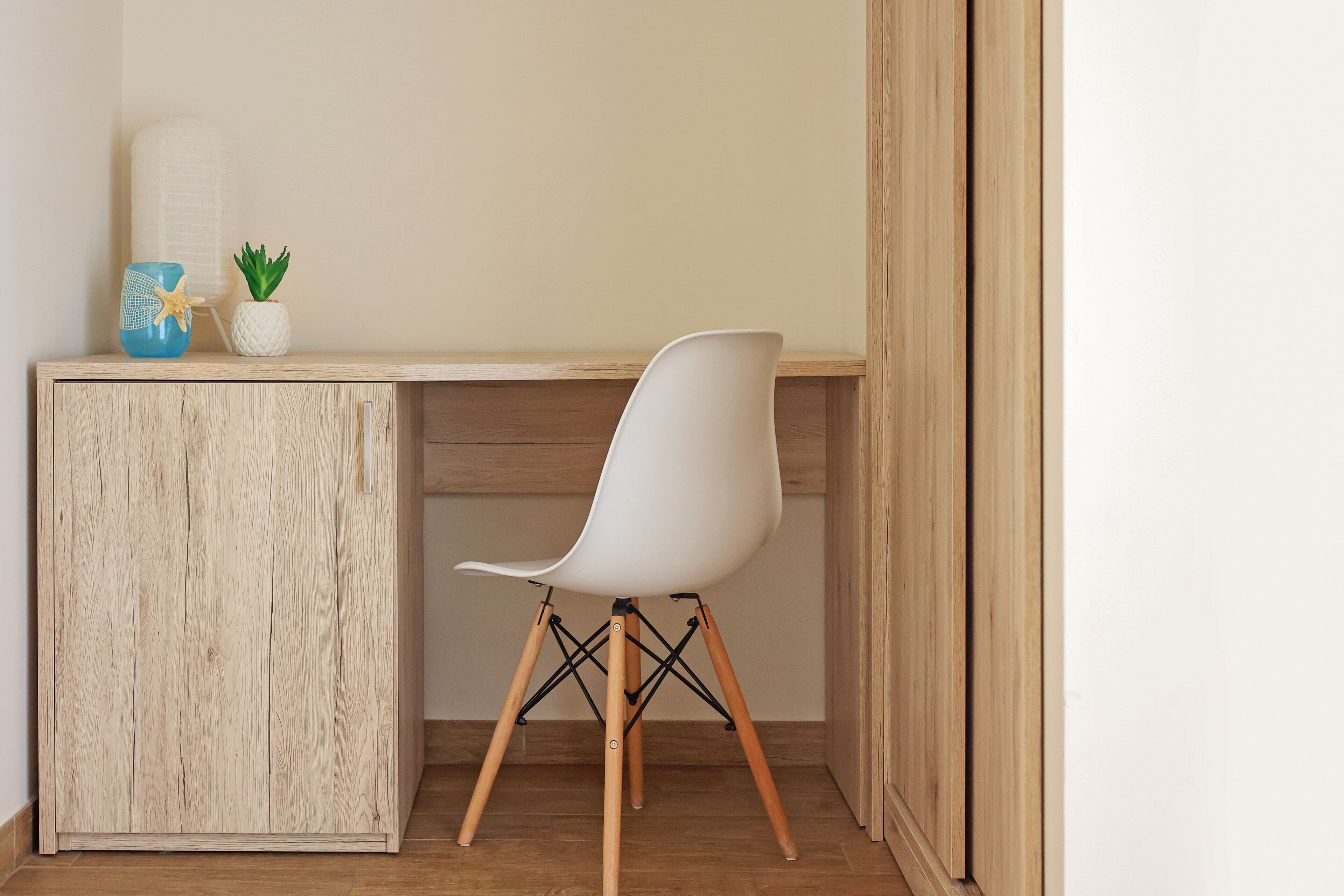 A wooden desk with a white chair, a blue vase with a starfish, and a small potted plant.