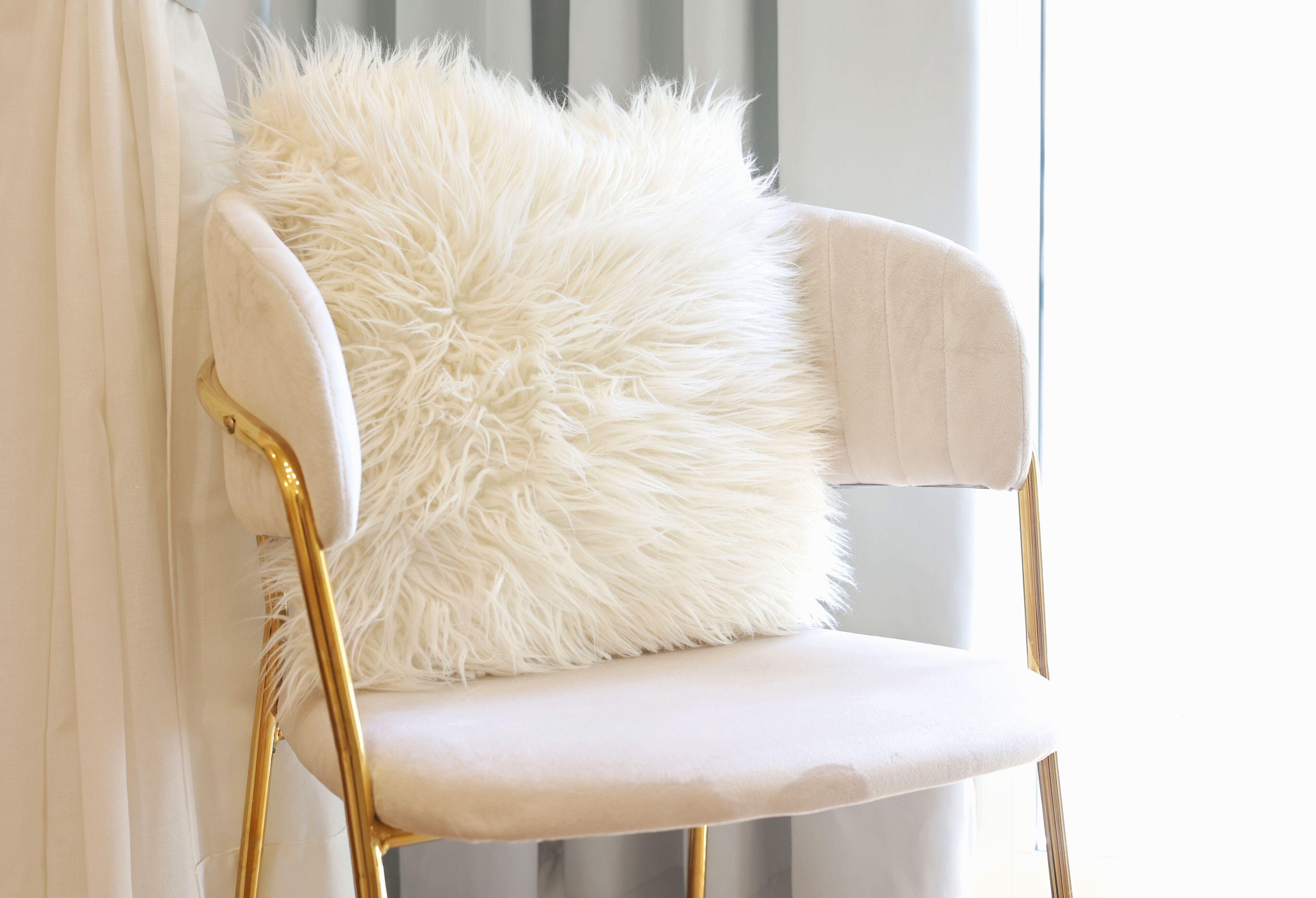 Une chaise blanche avec un coussin moelleux blanc et des pieds dorés.