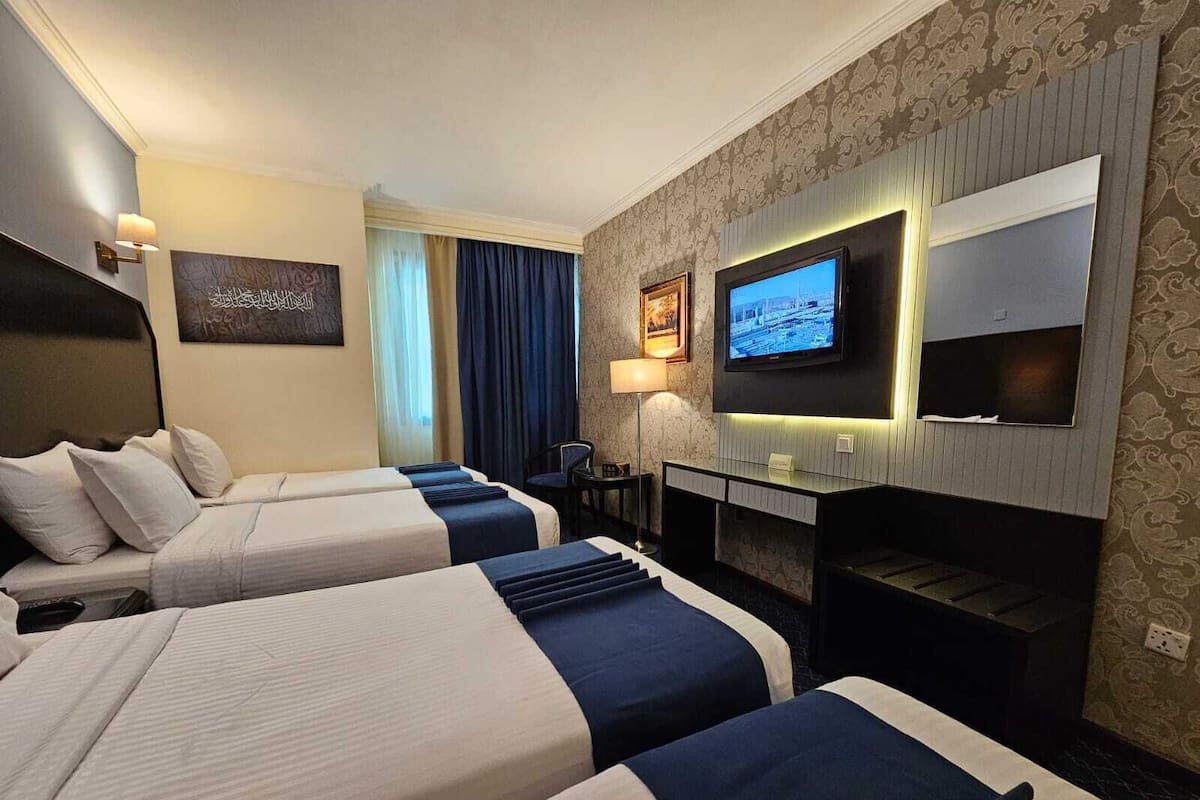 Une chambre d’hôtel avec deux lits, un bureau, une télévision et une fenêtre avec des rideaux.