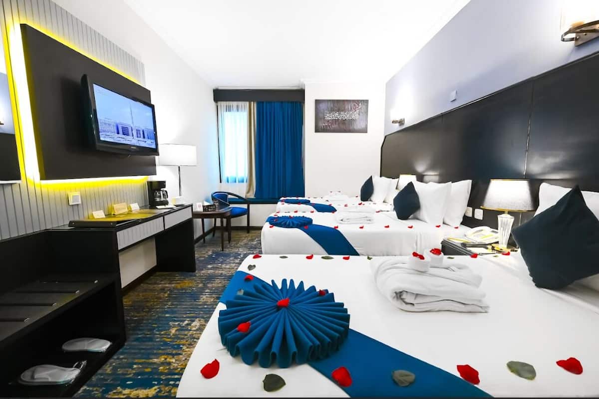 Une chambre d’hôtel avec deux lits, un bureau, une télévision et un grand élément décoratif placé au centre du lit.