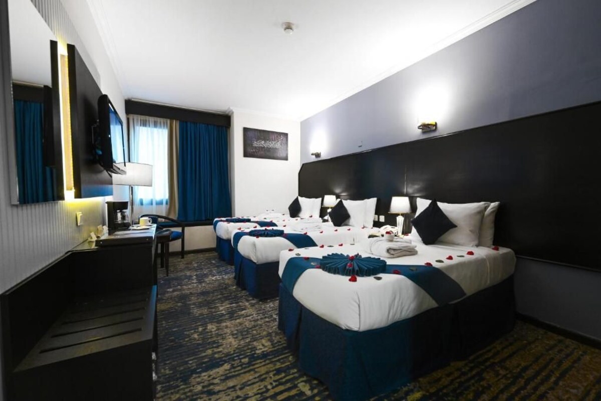 Habitación de hotel con cuatro camas, un escritorio, una silla, un televisor y un ventanal con cortinas.