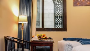 Une chambre d’hôtel avec un lit, un bureau doté d’une lampe, une chaise et un panier de fruits posé sur le bureau.