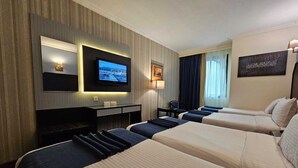 Une chambre d’hôtel avec deux lits, un bureau, une télévision et une fenêtre avec des rideaux.