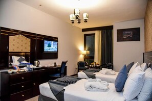 Two comfortable beds with crisp linens, a flat-screen TV, and a desk area with a chair.