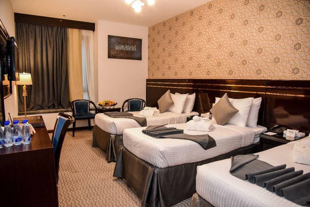 A hotel room with two beds, a desk with water bottles, a chair, and a small table with fruit.