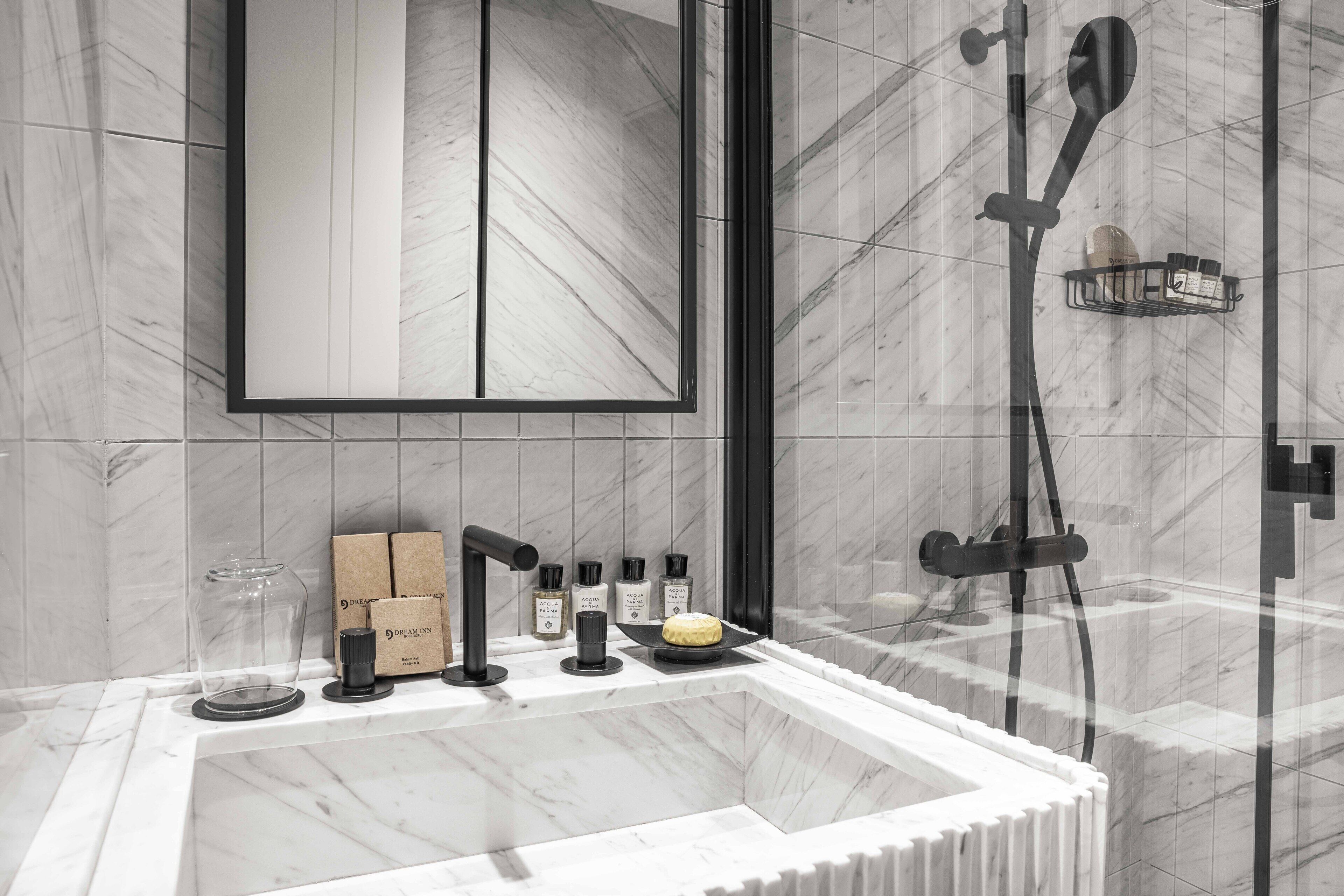 Une salle de bain moderne dotée d’un grand miroir, d’une douche avec un pommeau de douche amovible et d’un meuble-lavabo avec des articles de toilette.