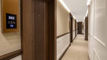 Un couloir d’hôtel avec des portes en bois, un écran numérique affichant le numéro de chambre 201 et un sol recouvert de moquette.