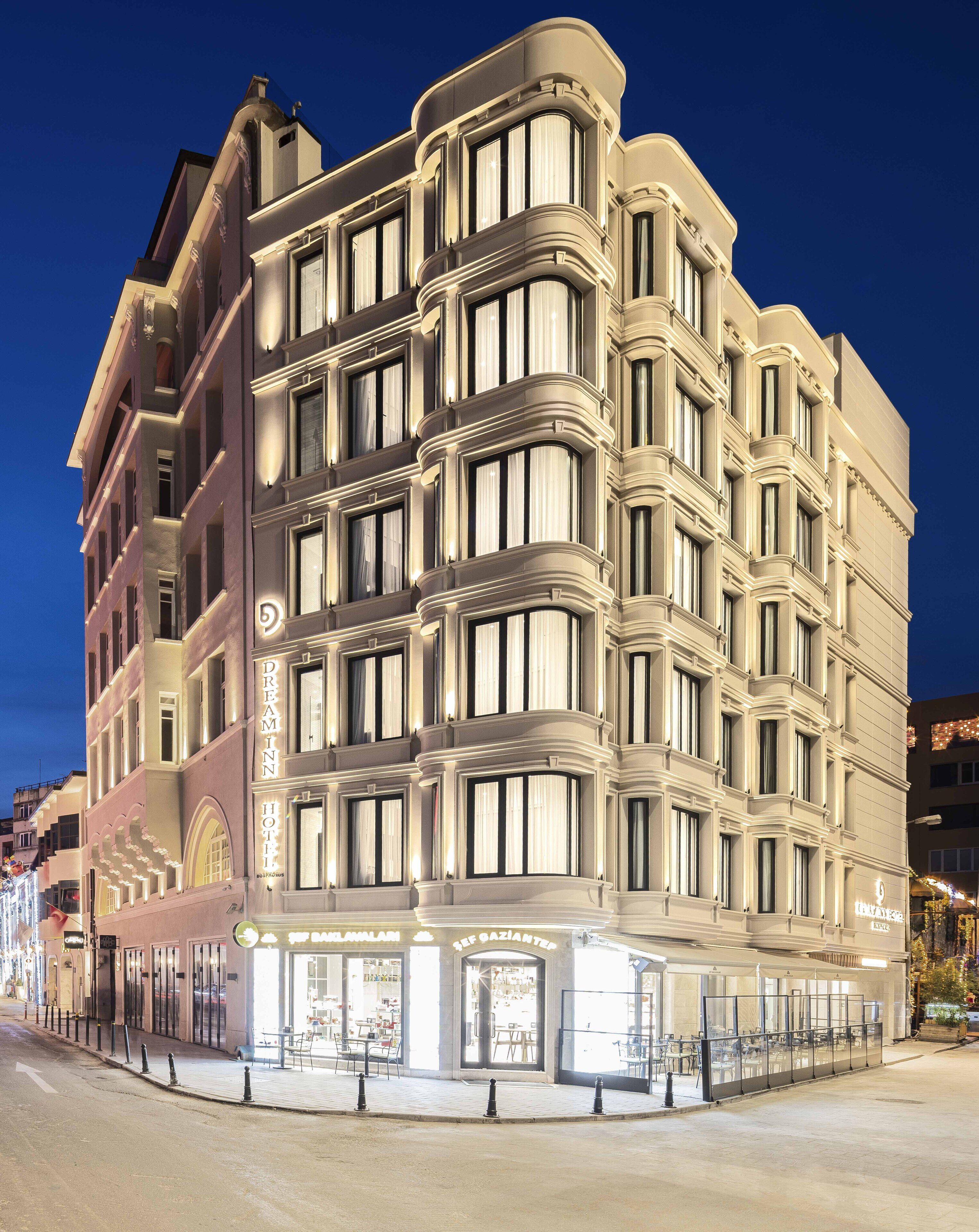 Un hôtel à plusieurs étages, doté d’une architecture classique, de grandes fenêtres et d’une entrée imposante avec une façade en verre.