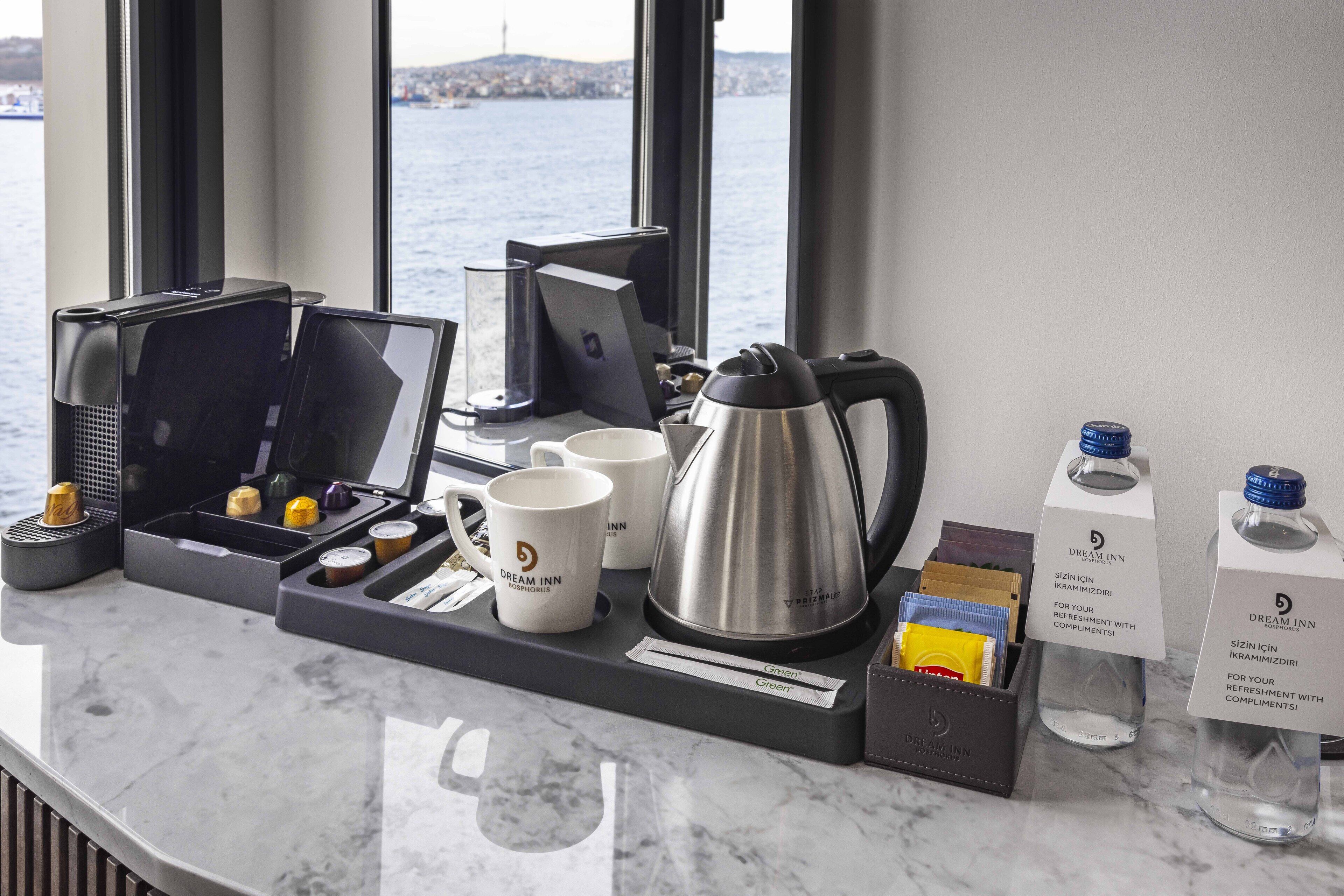 Un comptoir dans une chambre d’hôtel avec une machine à café, des tasses, un plateau avec des chocolats, une bouteille d’eau et une boîte aux couleurs de l’enseigne Dream Inn.