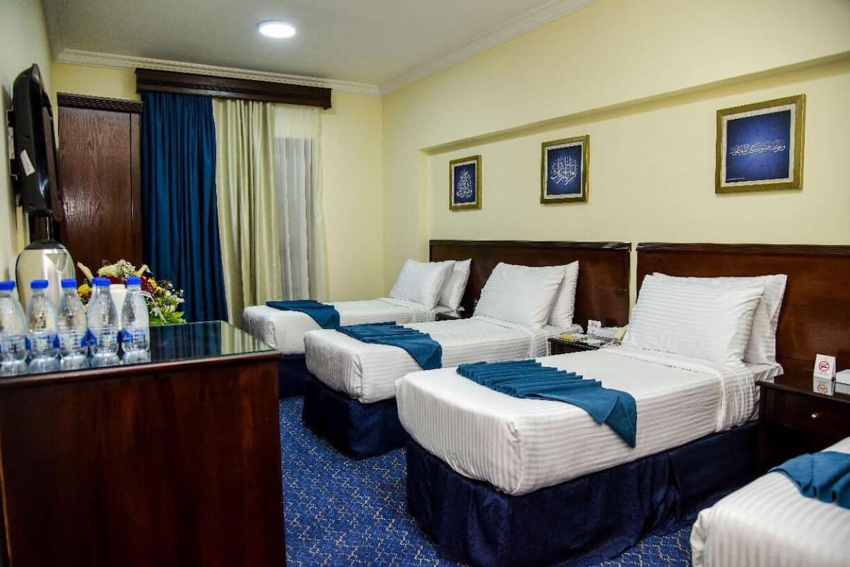 A hotel room with two beds, a desk with water bottles, and a coffee maker.