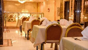 A dining area with tables set for service, chairs with white tablecloths, and a chandelier. - Plaza Inn Ohud (Madinah)