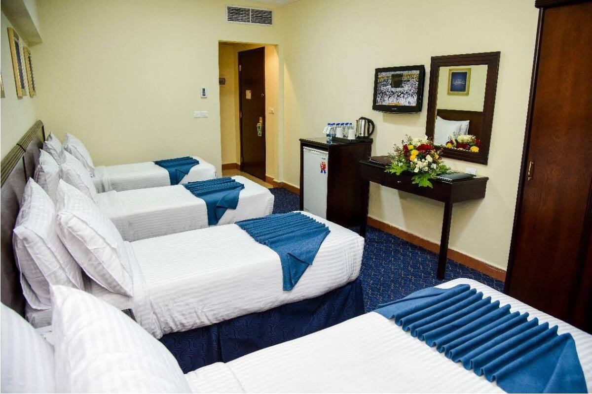 A hotel room with four beds, a desk with a coffee maker, and a small refrigerator.