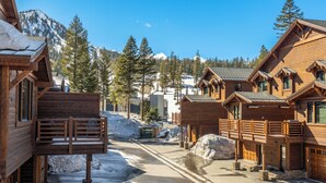 A wooden lodge with a balcony, a snow-covered street, and a mountain backdrop.