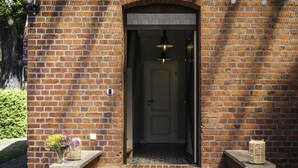 A brick entrance with a door, a hanging light fixture, and two small planters with flowers.