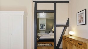 A narrow hallway leading to a bedroom with a bed, a nightstand, and a wooden cabinet.