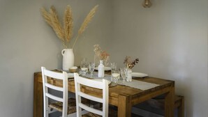 A dining table set with white chairs, a white vase with pampas grass, and various glassware.