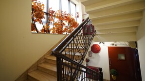 A staircase with a metal railing, a window with autumn leaves, and a red door. - Lyf Corporate Suites. New Friends Colony (New Delhi)