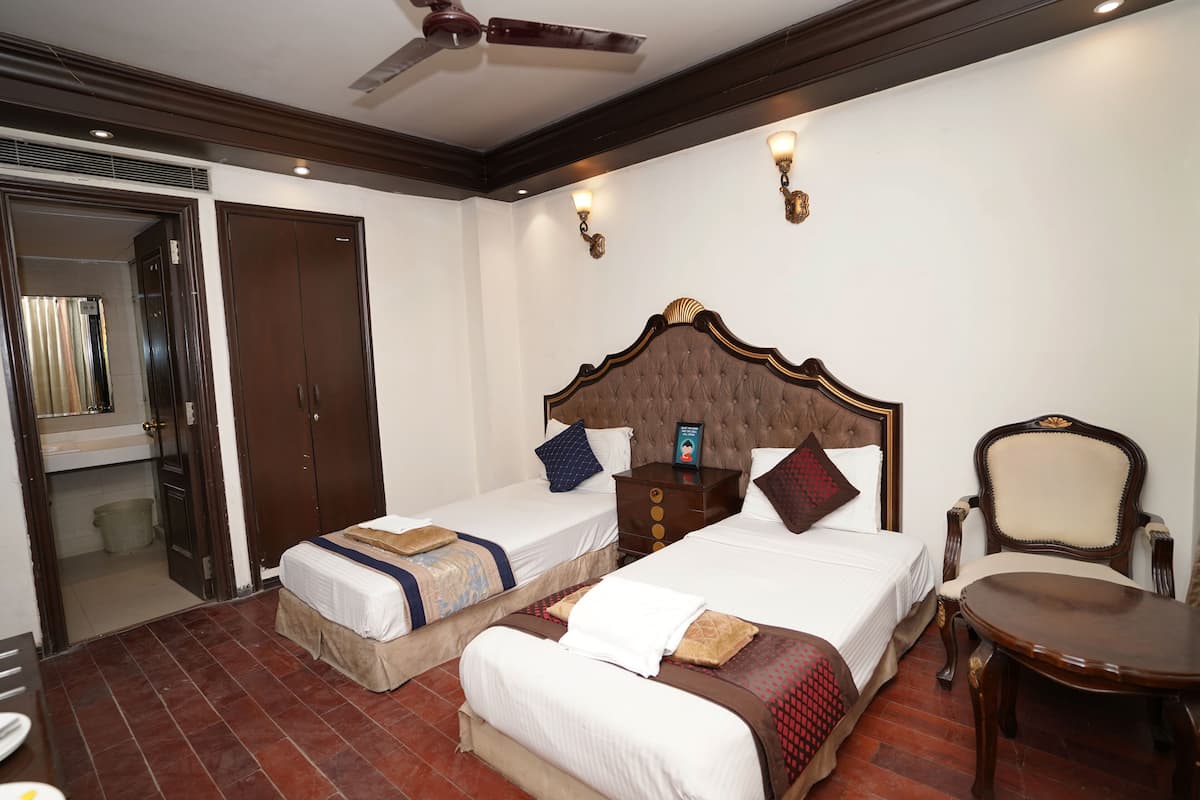 Ein Hotelzimmer mit zwei Betten, einem Holzstuhl, einem kleinen Tisch und einem Deckenventilator.