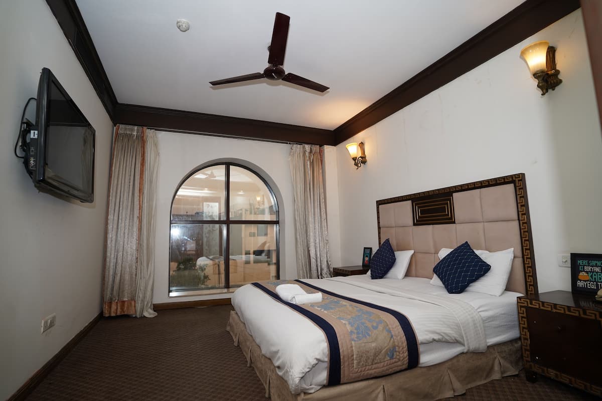 Ein Hotelzimmer mit einem großen Bett, einem Deckenventilator, einem Fernseher und Blick ins Freie durch ein großes Fenster.