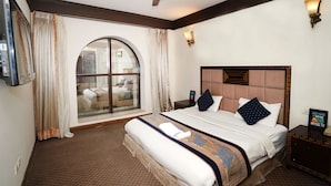 A hotel room with a large bed, a ceiling fan, a large window with curtains, and a wall-mounted light fixture. - Lyf Corporate Suites. New Friends Colony (New Delhi)