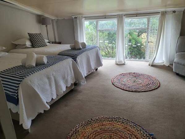 Habitación de hotel con dos camas, un ventanal grande con cortinas y una alfombra de lana de colores en el suelo.