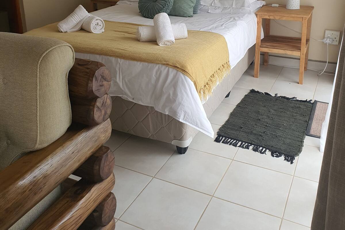 A bedroom with a bed, a bedside table, a fan, a nightstand, and a chair.