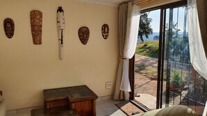 Habitació amb una banca de fusta, una taula petita i una porta corredissa de vidre que dona a un jardí.