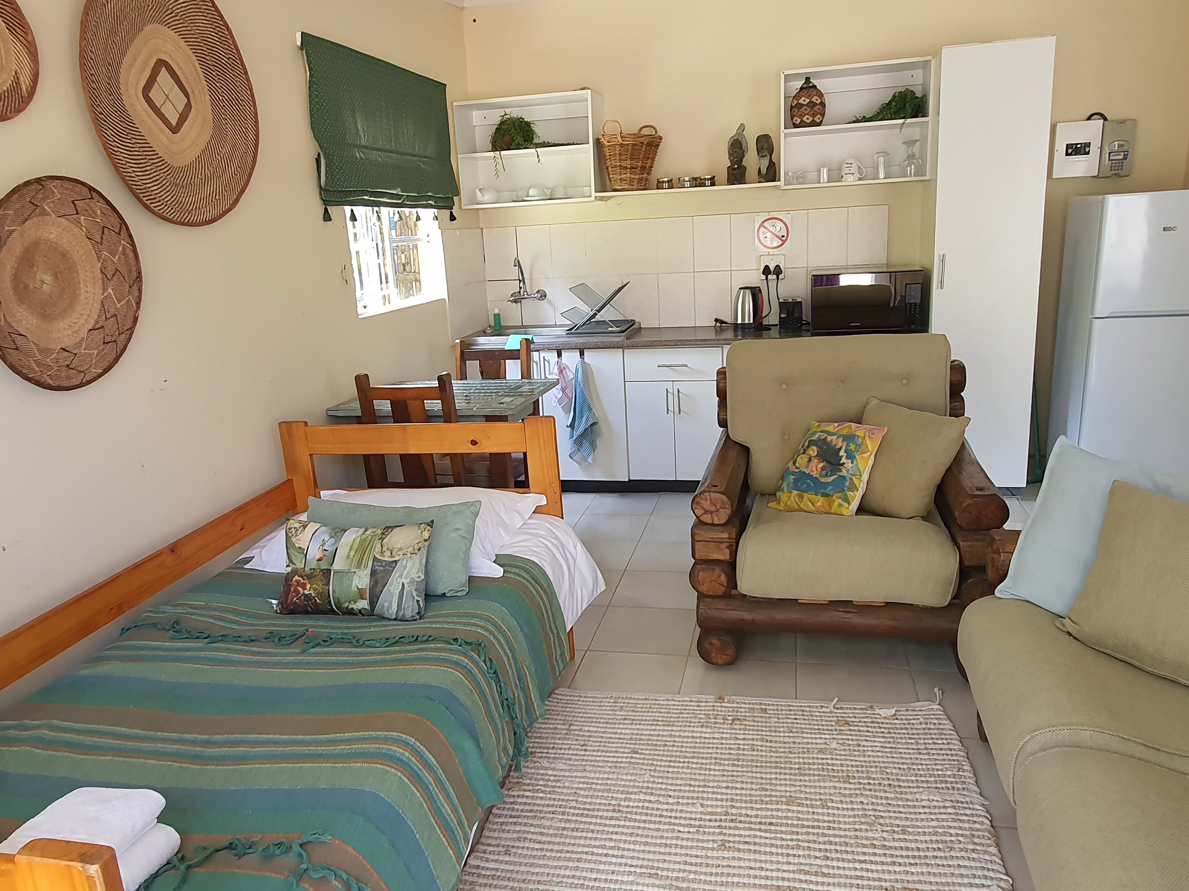 A compact living space with a bed, a sofa, a chair, a small kitchen area, and a refrigerator.