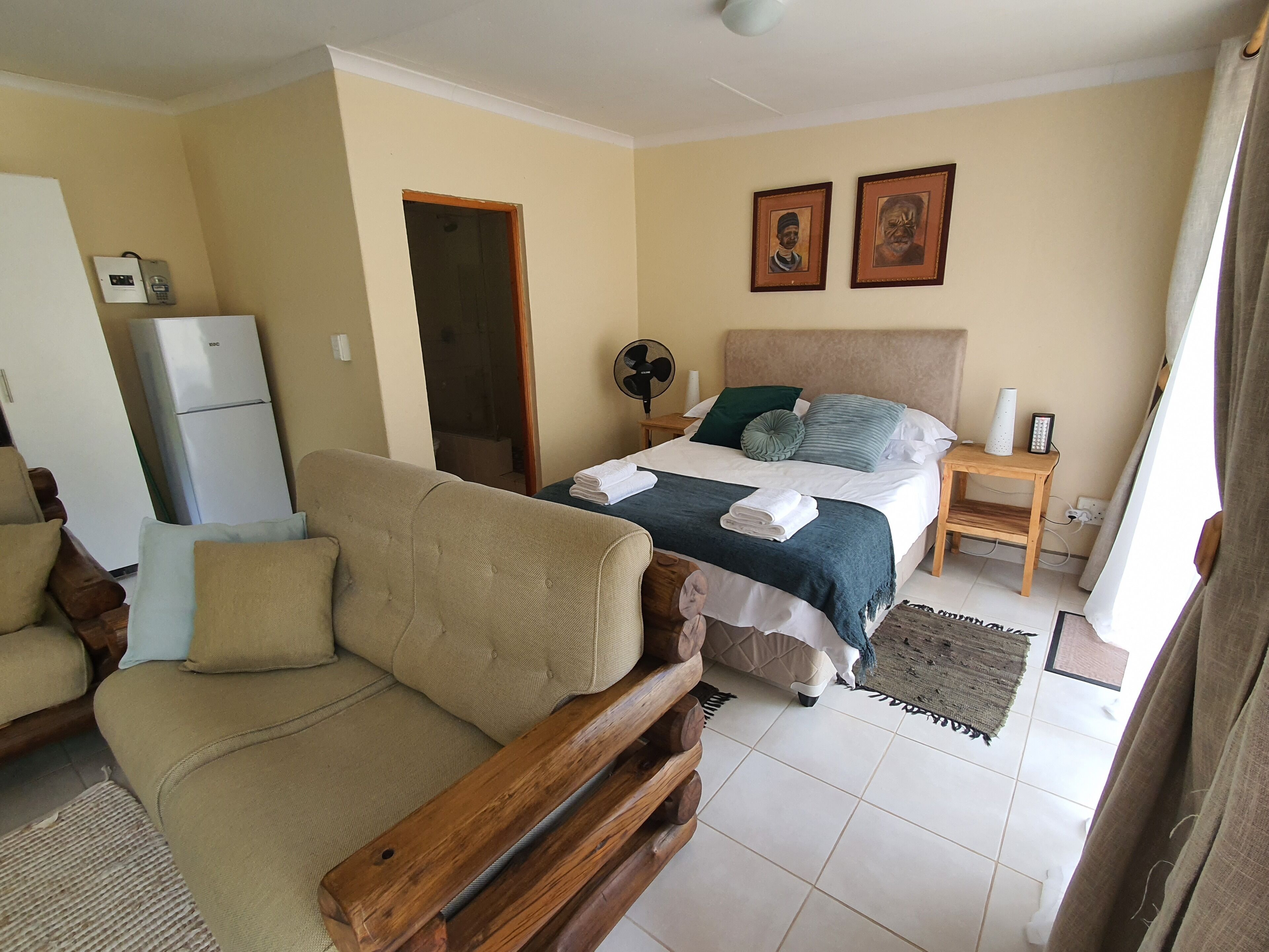 Ein Schlafzimmer mit Bett, Sofa, einer Holzbank, einem Ventilator und einem kleinen Tisch mit Lampe und Telefon.