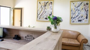 Et receptionsområde med et træskrivebord, en computer, en vase med blomster og en sofa. To abstrakte malerier hænger på væggen, og et skilt viser ordet 'KEYS'.
