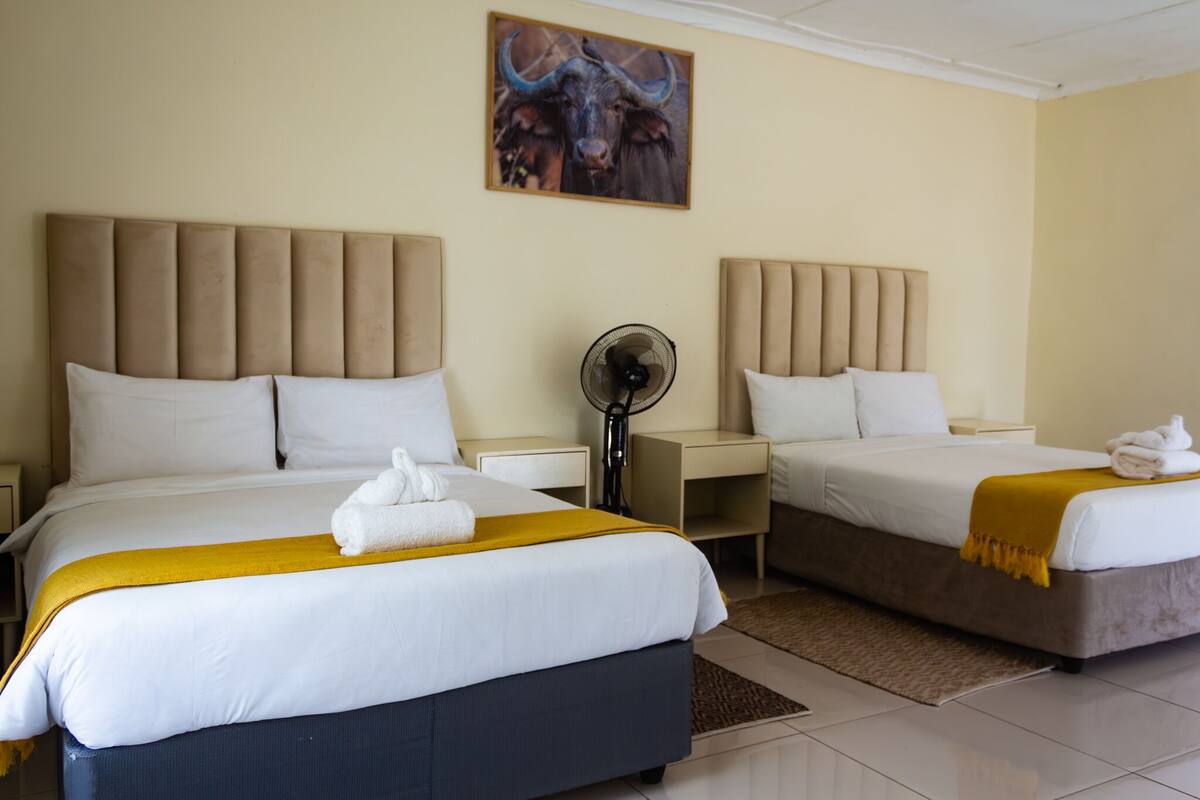 Quarto de hotel com duas camas, um ventilador e uma pintura de um touro na parede.