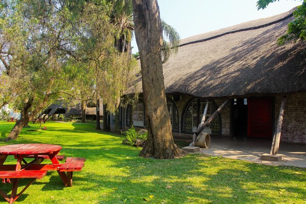 A picnic area with a thatched-roof building, a large tree, and a red picnic table.
