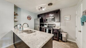 A modern kitchen with a central island, stainless steel appliances, and wooden cabinets. - River's Song Condo- Convenient for Walking (Helen)