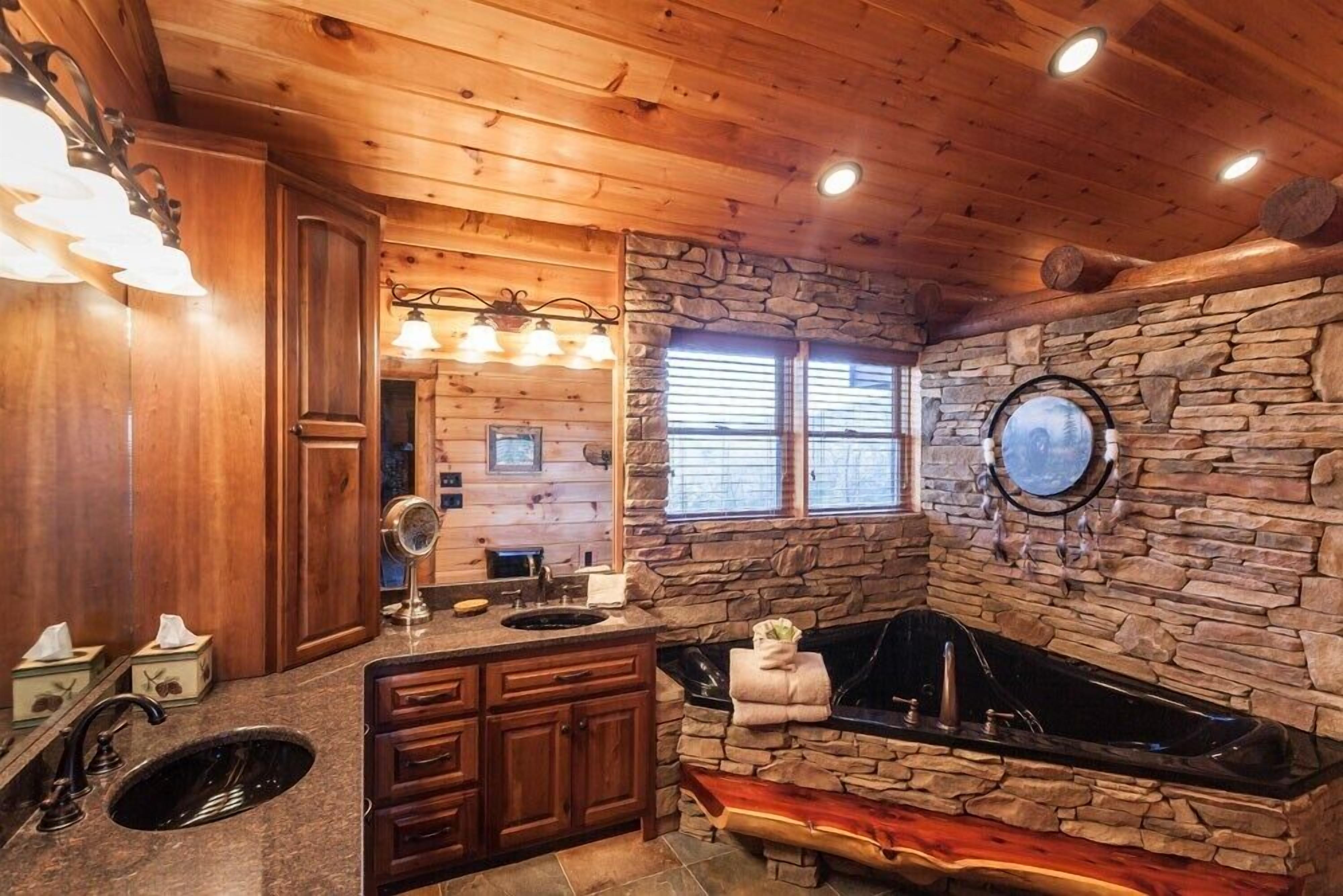 A wooden cabin bathroom with a stone wall, a sink, a vanity, and a bathtub.