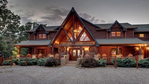 A log cabin with a prominent triangular roof, a front porch with seating, and a gravel driveway. - Five Star Lodge and Stables is pet friendly with a big mountain view. hot tub, firepits. Ideal for Weddings and Corporate Retreats (Morganton)