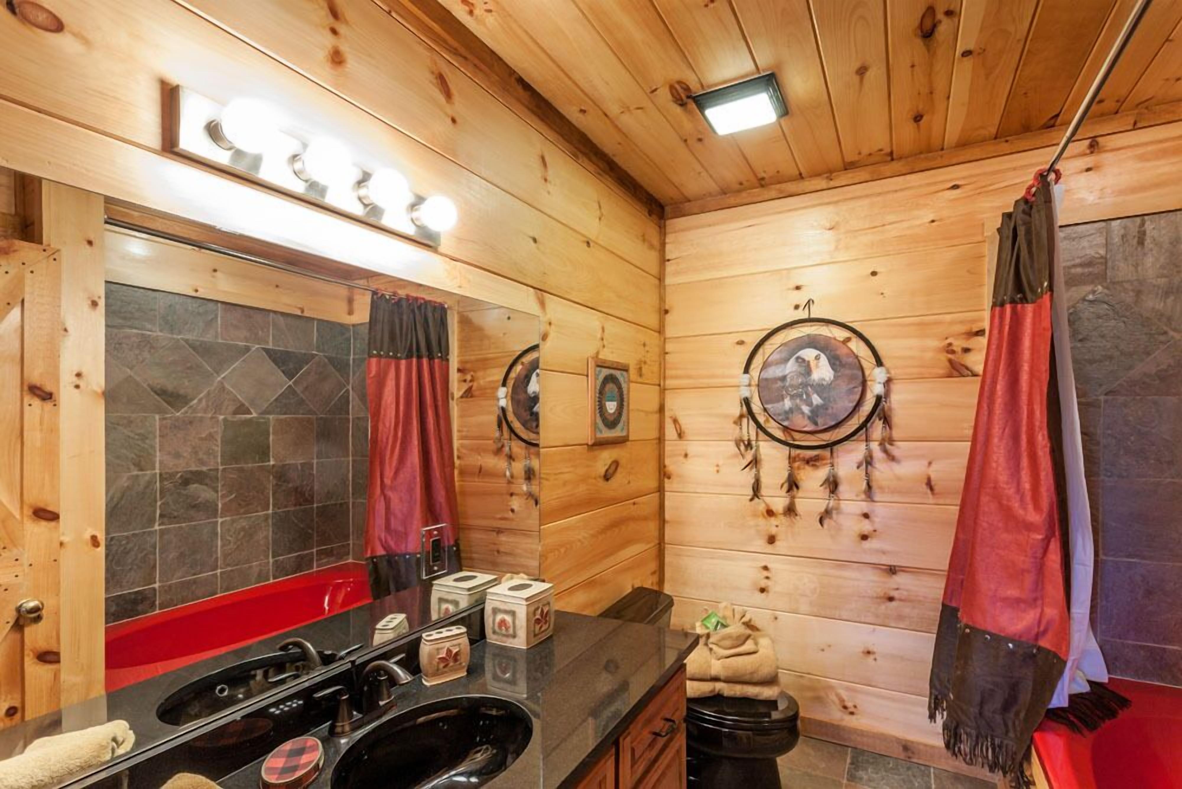Ein Badezimmer einer Holzhütte mit einem großen Spiegel, roten Vorhängen, einem Waschbecken und einer Toilette.