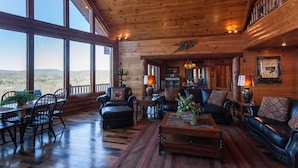 A spacious log cabin interior with a dining area, seating, and a large window offering a view of the outdoors. - Five Star Lodge and Stables is pet friendly with a big mountain view. hot tub, firepits. Ideal for Weddings and Corporate Retreats (Morganton)