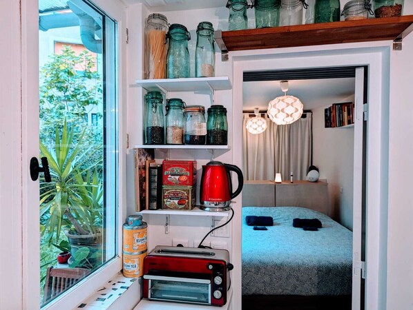 A compact kitchen with a toaster, a red kettle, and various jars on shelves. - ღ LE JARDIN PARISIEN - quiet with terrace wifi, video projector (Paris)