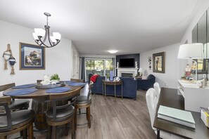 A modern living room with a dining area, a fireplace, and a TV mounted on the wall.