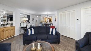 Ein Wohnzimmer mit einem dunkelblauen Sofa, Holzschränken, einem Essbereich und einer Küche im Hintergrund.