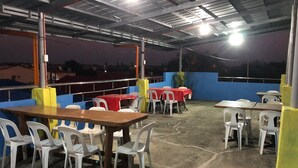 An outdoor patio area with tables and chairs, a blue wall, and a view of the cityscape at dusk. - RAVARA-NATIVIDAD PENSION HOUSE (Alaminos)