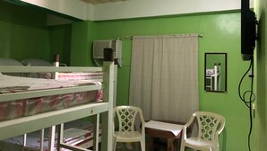 A room with bunk beds, a small table, two chairs, a mirror, and an air conditioning unit. - RAVARA-NATIVIDAD PENSION HOUSE (Alaminos)