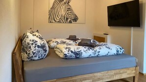 Un dormitorio con cama, almohadas estampadas, una obra de arte con cebra y un televisor en la pared.