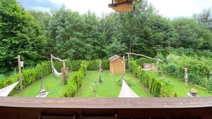 Una terraza de madera con vistas a un jardín cuidado, un conjunto de columpios y una pequeña estructura de madera.