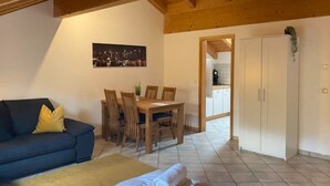 A cozy living room with a sofa, a dining table with chairs, a bed with pillows, a painting on the wall, and a wardrobe. - Schöne Ferienwohnung "hubertus" im Dachgeschoss (Holzkirchen)