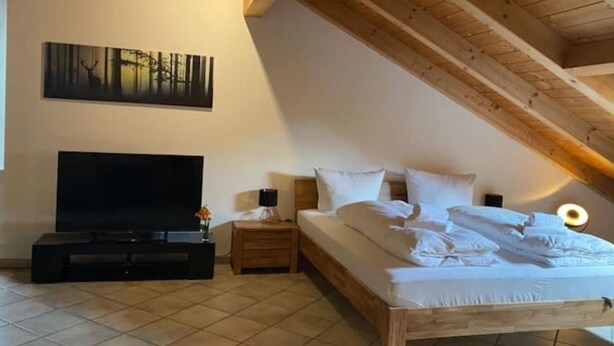 A bedroom with a wooden ceiling, a bed, a TV, and a painting on the wall. - Schöne Ferienwohnung "hubertus" im Dachgeschoss (Holzkirchen)