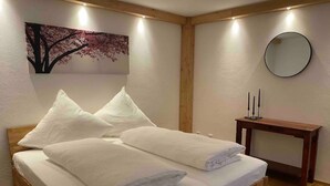 A bedroom with a wooden bed, white pillows, a wooden bedside table with candles, a wall-mounted mirror, and a painting of a tree. - Neurenovierte 60m2 Fewo Xaverl zw. Stadt&bergen (Holzkirchen)