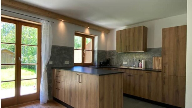 A modern kitchen with wooden cabinets, a central island, and a large window. - Neurenovierte 60m2 Fewo Xaverl zw. Stadt&bergen (Holzkirchen)