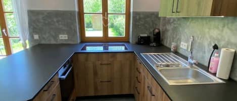 A modern kitchen with wooden cabinets, a black countertop, a built-in sink, and a window with a view of greenery.